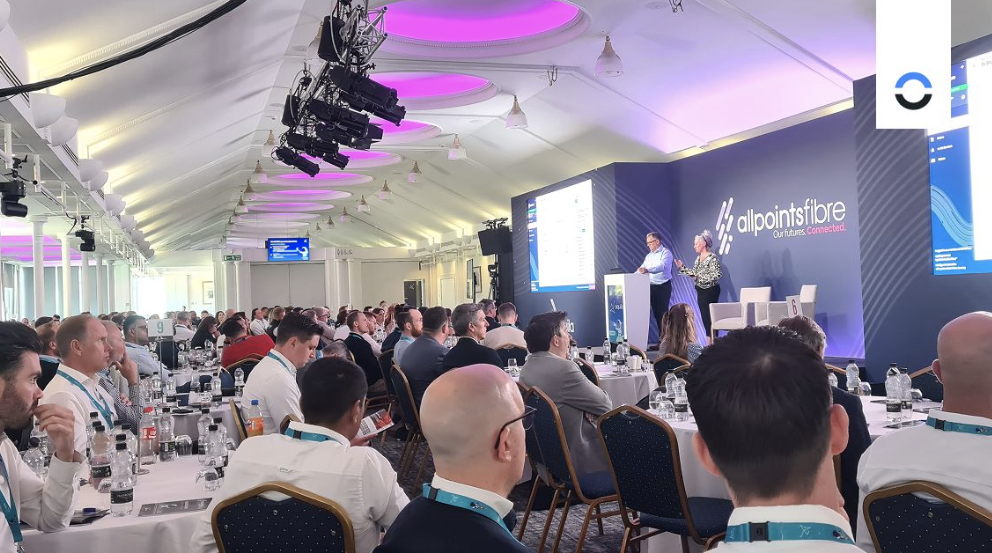 Audience at the aquila launch event onference room full of attendees seated at round tables listening to speakers on stage at the AllPoints Fibre aquila launch, with event branding on the screen and backdrop.
