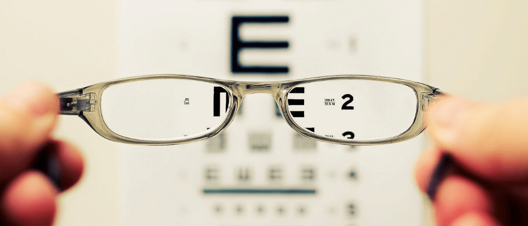 Eye test chart viewed through a pair of glasses that are being held aloft
